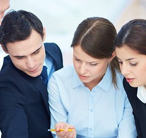 Three business colleagues looking intently at documents, one pointing with a pen.