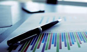 Pen rests on a business chart with colorful bar graphs, office setting.