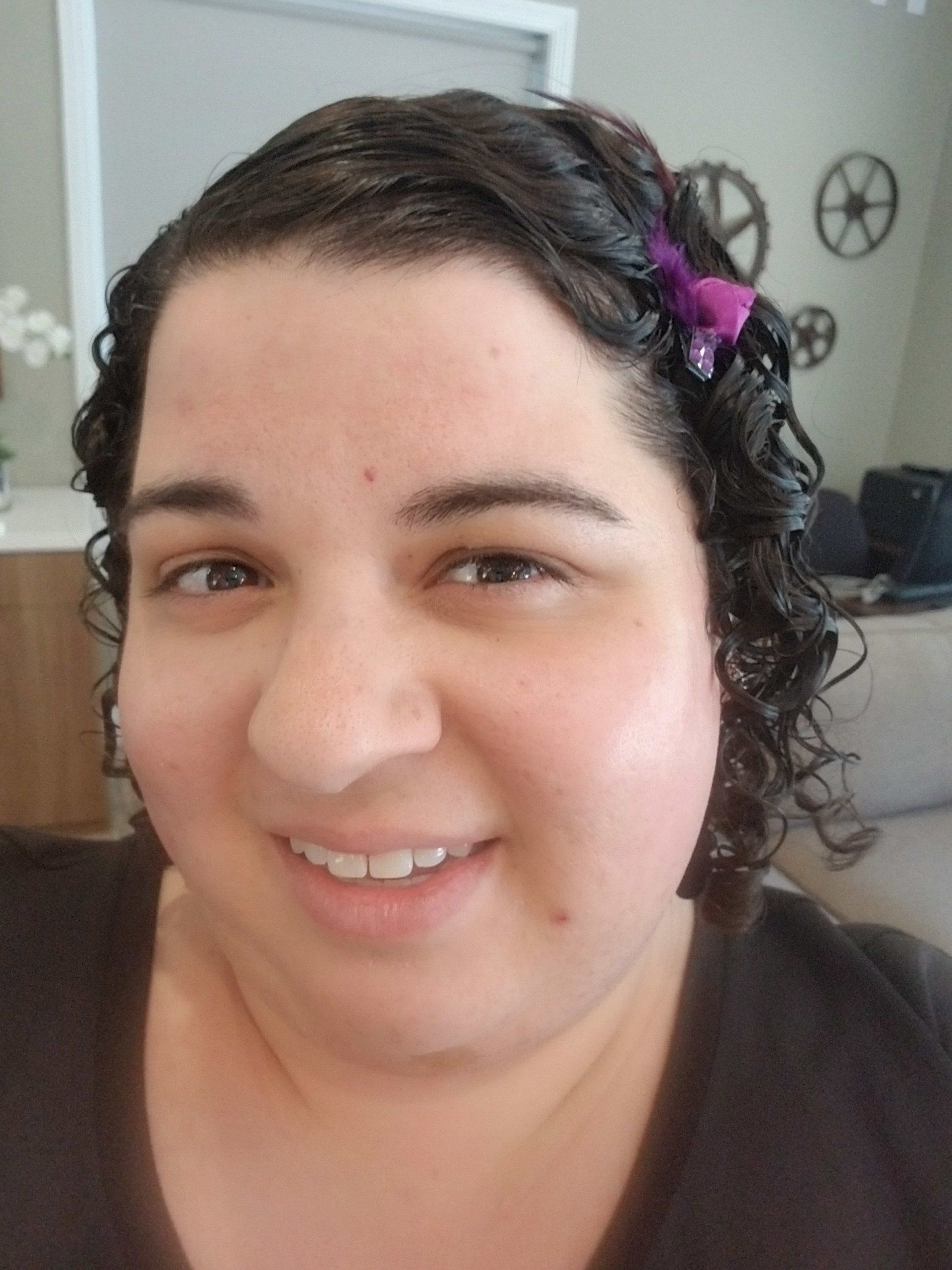 Woman with dark curly hair and purple hair clip smiling indoors.