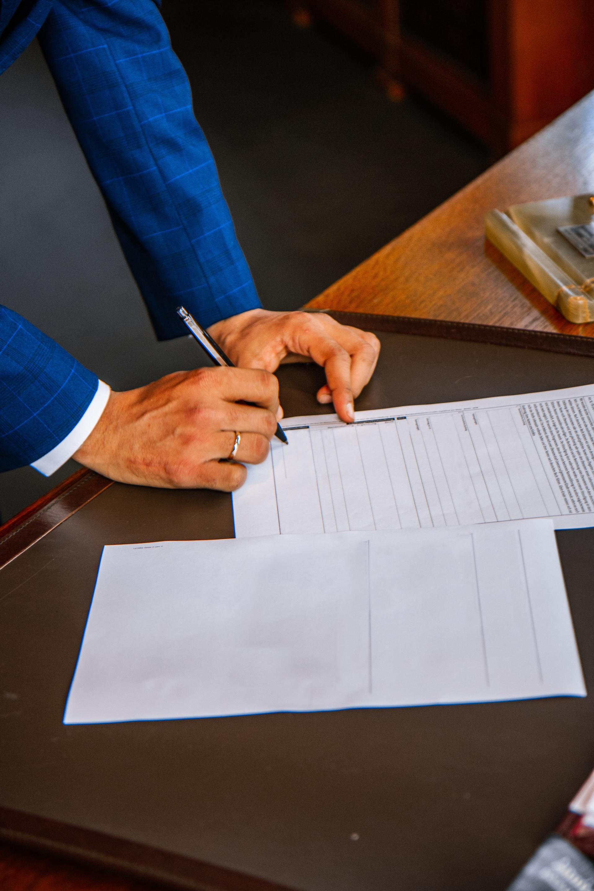 Person in blue suit signing a document on a desk with a pen.